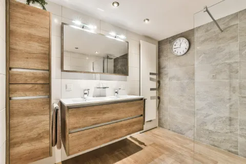 Saniertes Bad mit bodengleicher Dusche, großen Fliesen und Waschtisch aus Holz